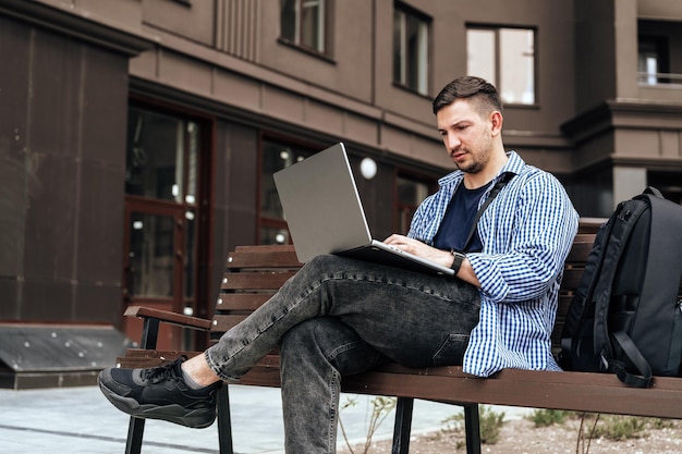Jonge man die aan een laptop werkt terwijl hij buiten op een bankje zit