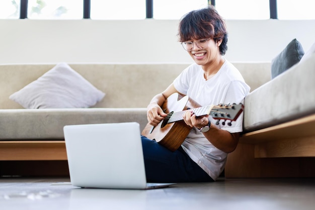 Jonge man die akoestische instrumentale gitaar speelt en op de vloer zit in een woonhuis thuis