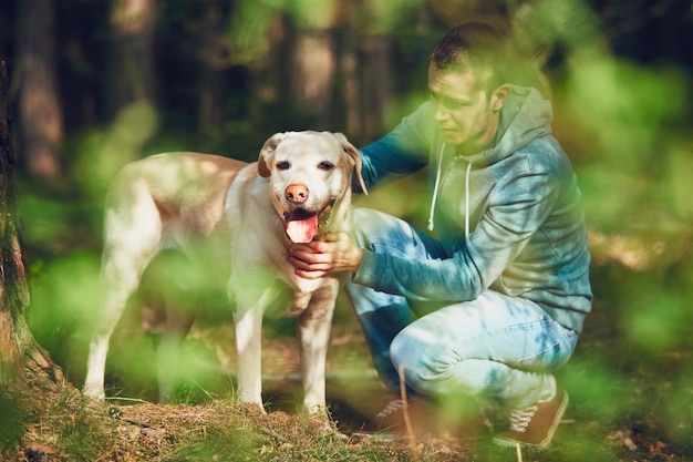Jonge man die bij een hond op het veld in het bos kruipt