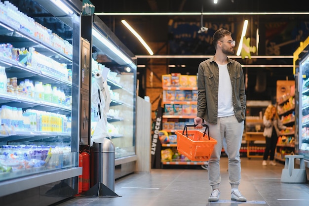 Jonge man die boodschappen koopt in de supermarkt Andere klanten op de achtergrond Consumerisme concept