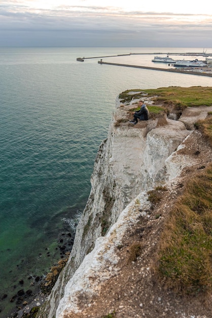 Jonge man die de White Cliffs of Dover in het VK verkent. Zittend op de top van de klif kijkend naar het Engelse kanaal.