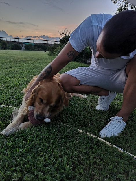 Foto jonge man die een hond aaien op een grasveld tegen de lucht in het park tijdens de zonsondergang