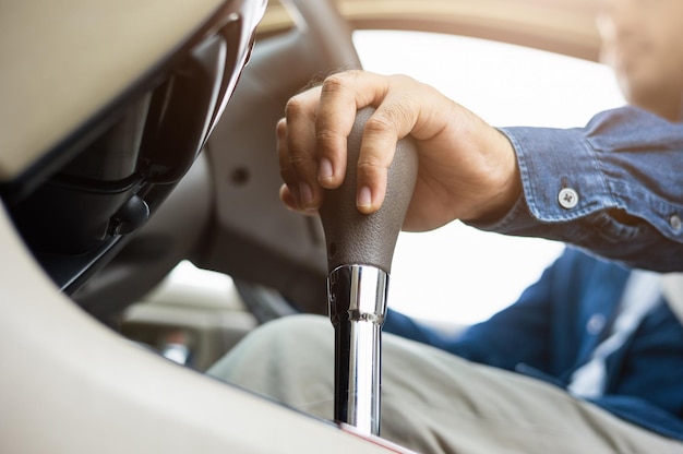 Foto jonge man die een nieuwe auto krijgt en zijn hand de stick shift-transmissie in luxe auto bestuurt