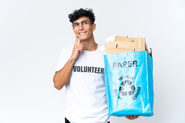 Jonge man die een recyclingzak vol papier houdt die een idee denkt terwijl hij omhoog kijkt