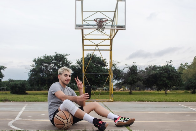 Jonge man die een selfie maakt en het vredesteken maakt op een verlaten basketbalveld.