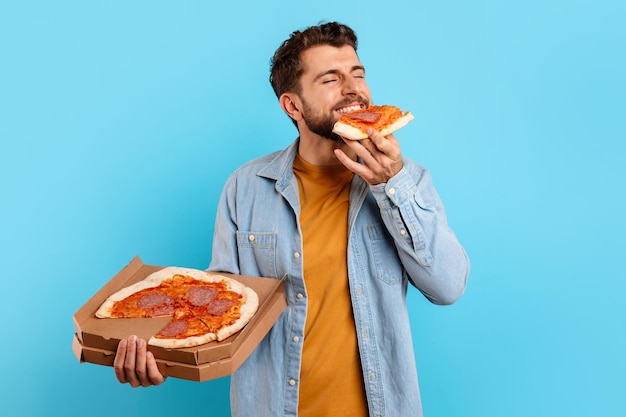 Jonge man die een stuk pizza eet en poseert met een doosstudio