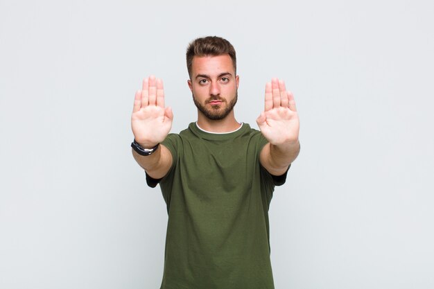 Jonge man die ernstig, ongelukkig, boos en ontevreden kijkt en de toegang verbiedt of stop zegt met beide open handpalmen