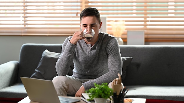 Jonge man die koffie drinkt en computerlaptop op de bank gebruikt