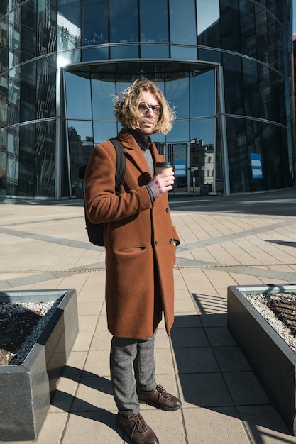 Jonge man die koffie drinkt terwijl hij buiten op straat staat