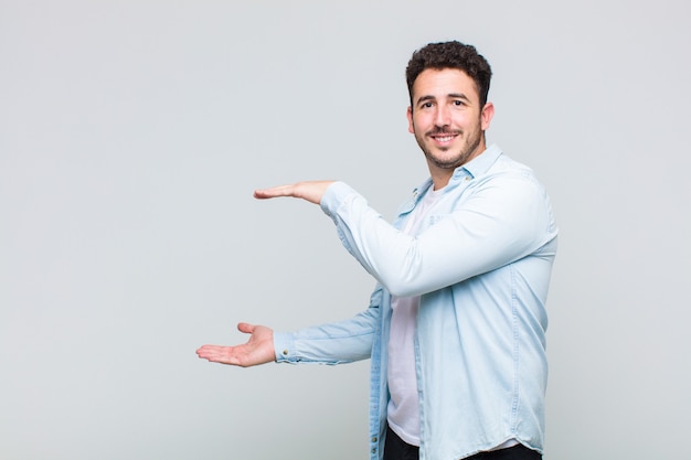 Jonge man die lacht, zich gelukkig, positief en tevreden voelt, object of concept op kopie ruimte vasthoudt of toont