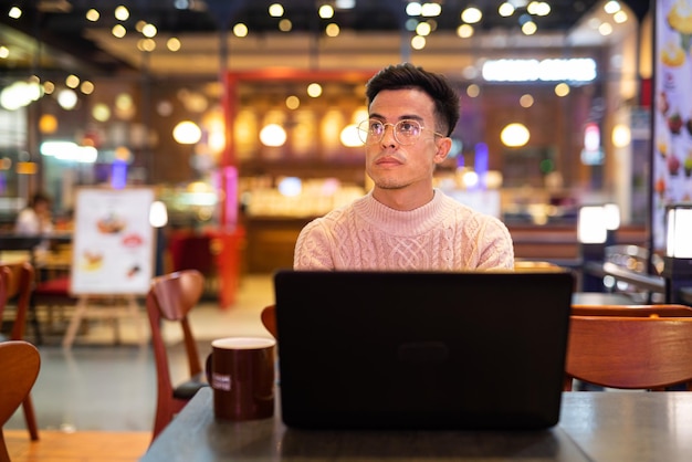 Jonge man die laptopcomputer gebruikt in de coffeeshop terwijl hij nadenkt