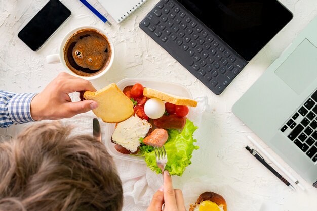 Foto jonge man die maaltijd voor de laptop neemt tijdens het werken, concepten voor slechte gewoontes en obesitas