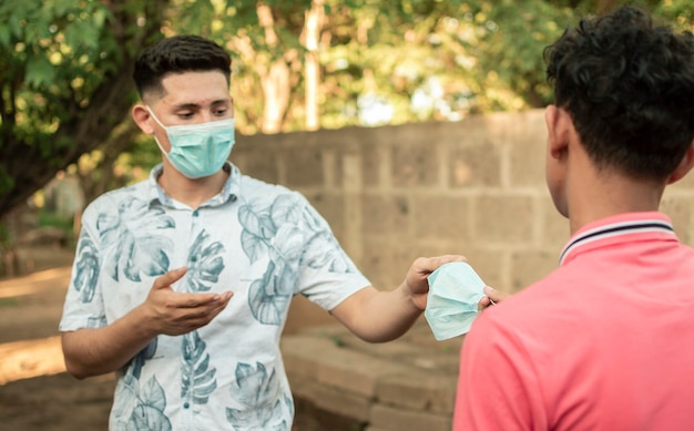 Jonge man die masker deelt met een andere jonge man, jonge man die een masker geeft aan een andere jonge man, concept van het geven van een masker,