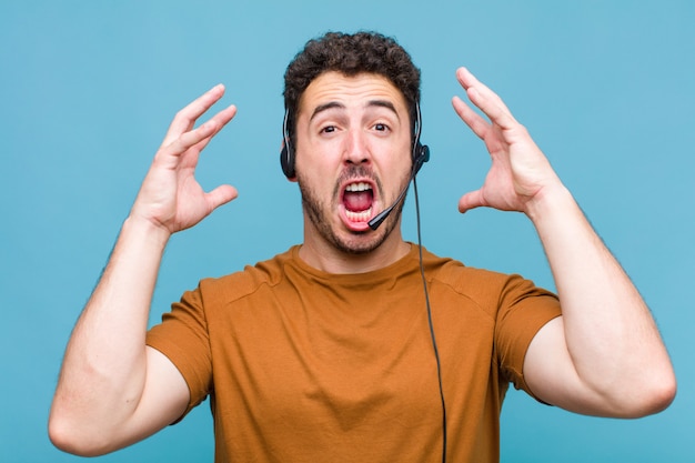 Jonge man die met de handen in de lucht schreeuwt, zich woedend, gefrustreerd, gestrest en boos voelt