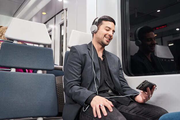 Foto jonge man die met zijn mobiele telefoon in de metro zit en naar muziek luistert
