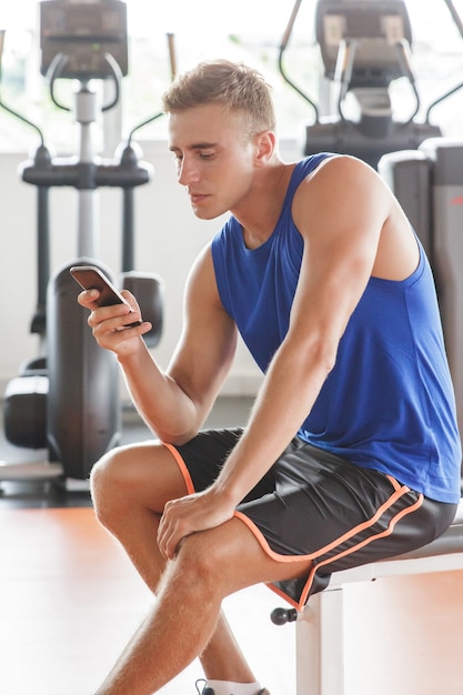 jonge man die mobilofoon speelt terwijl hij een pauze neemt tijdens de training in de sportschool