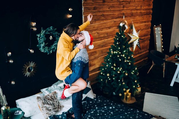 Jonge man die mooie gelukkige vrouw vasthoudt en kust in de buurt van kerstversieringen