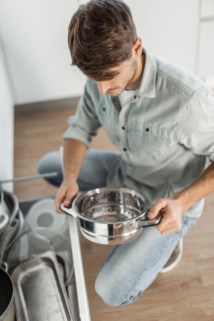 Jonge man die naar schone vaat in de vaatwasser kijkt