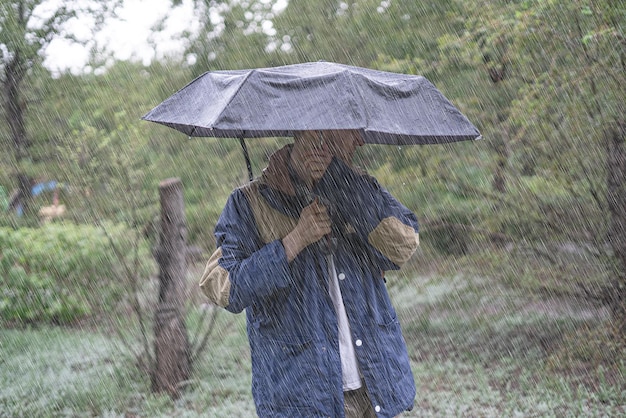 Jonge man die onder de paraplu staat, beschermt tegen zware tropische regenval in bossen