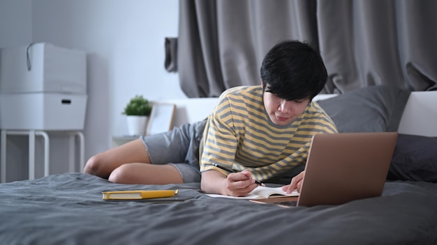 Jonge man die op bed ligt en online werkt of studeert met een computerlaptop