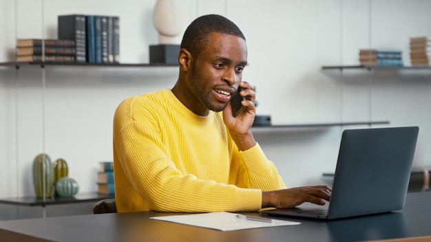 Jonge man die op de smartphone praat terwijl hij aan het bureau zit