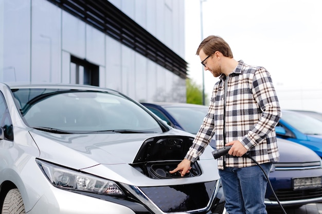 Jonge man die oplaadkabel in de auto-aansluiting steekt Elektrische auto opladen concept