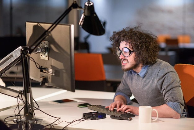 Jonge man die 's nachts op de computer werkt in een donker startkantoor. De ontwerper werkt in de latere tijd.