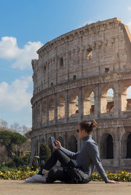 Jonge man die smartphone gebruikt en zit te rusten in het Colosseum in Rome, Italië