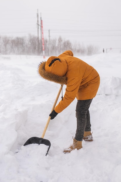 Foto jonge man die sneeuw opruimt in zijn achtertuin met een schop verwijdert sneeuw van het trottoir