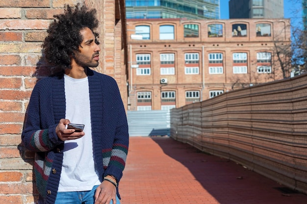 Jonge man die tegen een bakstenen muur staat en een telefoon gebruikt