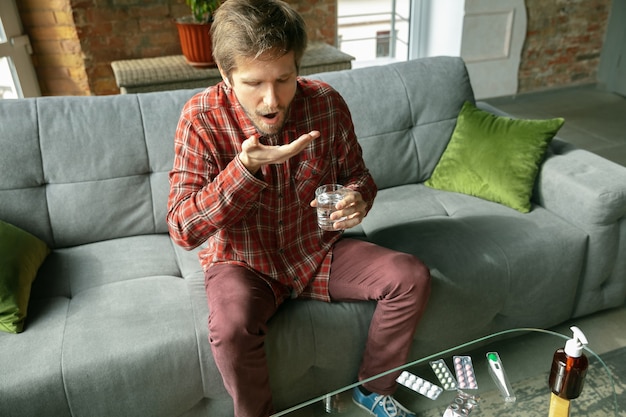 Jonge man die thuis blijft, water drinkt en pillen slikt