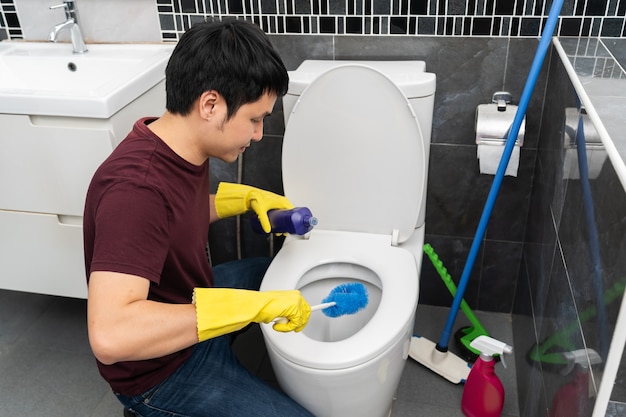 Jonge man die toiletpot in de badkamer schoonmaakt