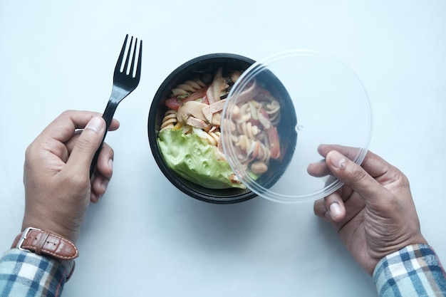 Jonge man die verse groentesalade eet in een plastic kom