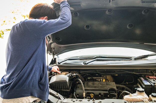 Jonge man die vloeibare auto voor de motor controleert en de motorkap opheft