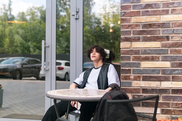 Jonge man die wacht op iemand die aan een tafel in een buitencafeteria zit