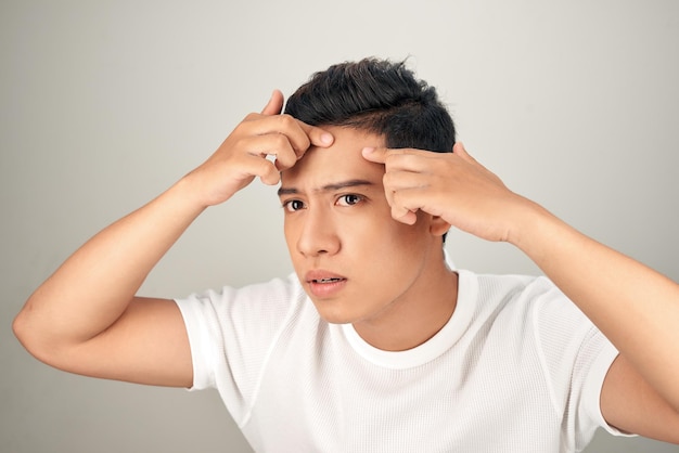 Jonge man die worstelt met acne op zijn gezicht die voor zijn huid zorgt, duwt acne weg