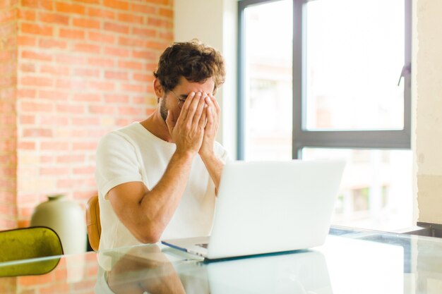 Jonge man die zich verdrietig, gefrustreerd, nerveus en depressief voelt, gezicht met beide handen bedekt, huilt