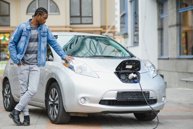 Jonge man die zijn elektrische auto wacht om te worden opgeladen