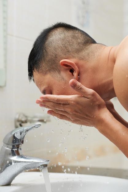 Jonge man die zijn gezicht afspoelt met kraanwater om 's ochtends het reinigingsmiddel in de badkamer af te wassen