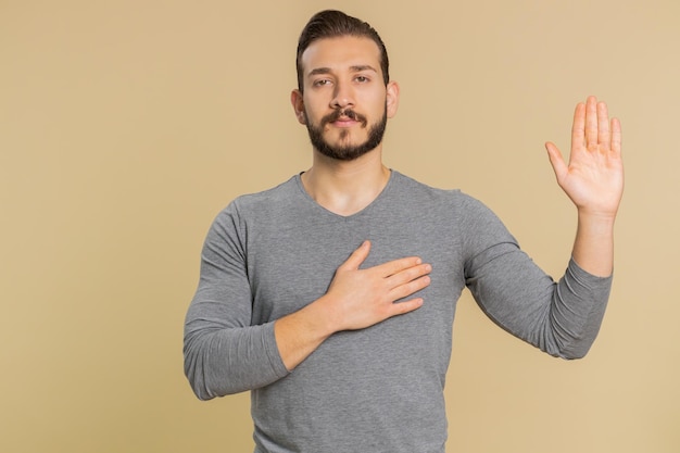 Jonge man die zijn hand opheft om de eed af te leggen, die belooft eerlijk te zijn en de waarheid te vertellen, met zijn hand op zijn borst.