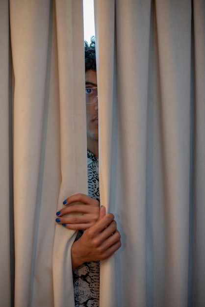 Jonge man die zijn identiteit verbergt terwijl hij door een opening in het gordijn kijkt