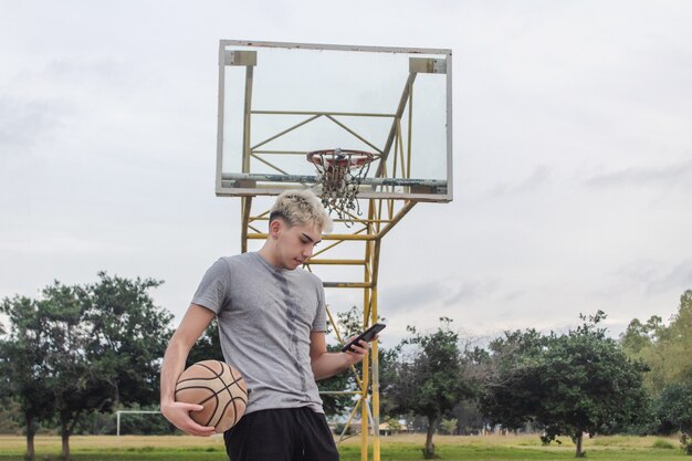 Jonge man die zijn smartphone gebruikt vanaf een verlaten basketbalveld.