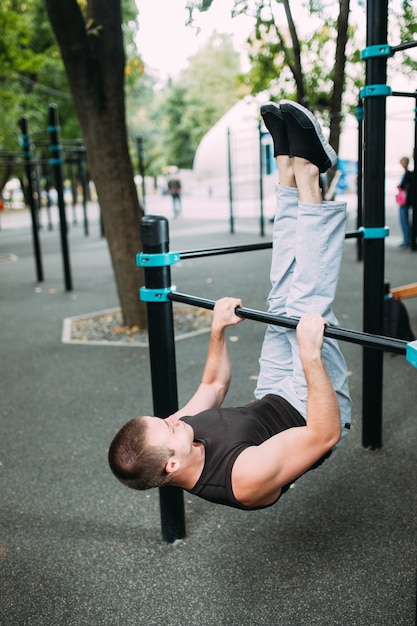 Jonge man doet pull-ups op rekstok buitenshuis, training, sportconcept.