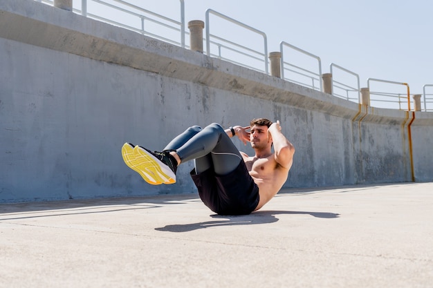 Jonge man doet sit-ups zonder shirt op straat 's middags