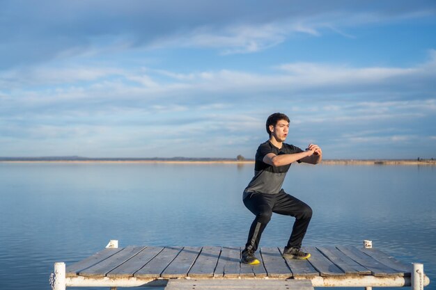 Jonge man doet squats op de pier van een meer