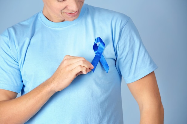 Jonge man draagt t-shirt met blauw lint op kleur achtergrond close-up Prostaatkanker bewustzijn concept