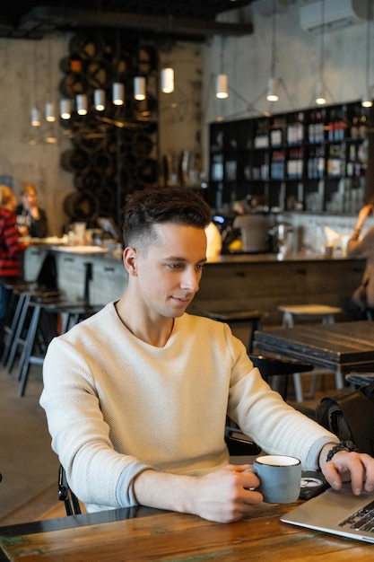 jonge man drinkt thee en werkt op een laptop, freelancer werkt in een café
