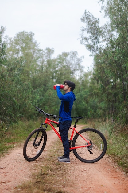 Jonge man drinkwater op zijn fiets op een bosweg, actieve levensstijl.