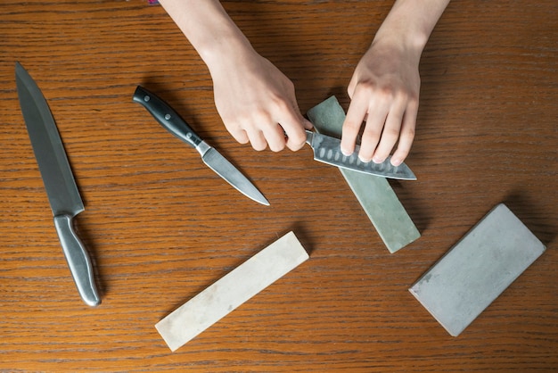 Foto jonge man een mes slijpen op houten tafel op donkere achtergrond b