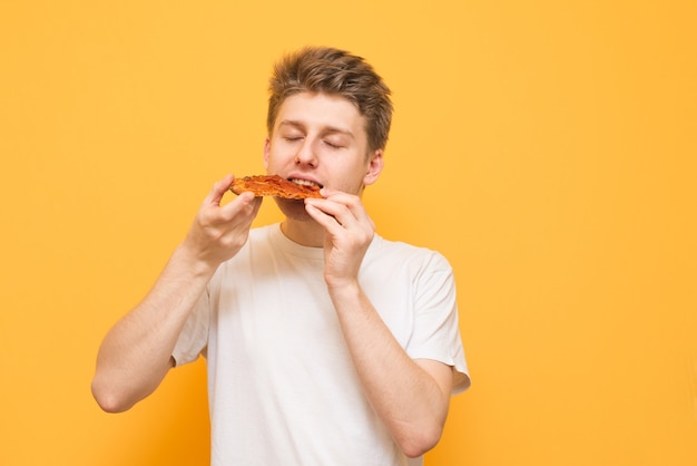 Jonge man eet een stuk smakelijke pizza op een gele